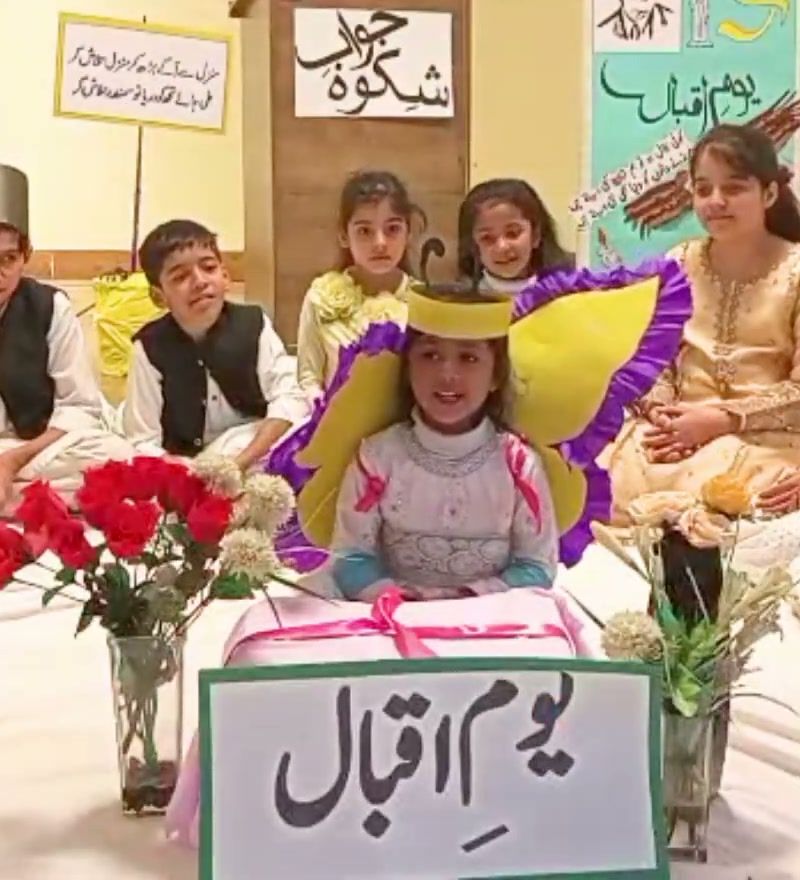 Pupils in traditional dress sitting in a circle to recite poetry at the school's Iqbal Day celebration