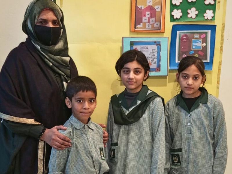 A teacher standing with three of her pupils in front of their classroom display