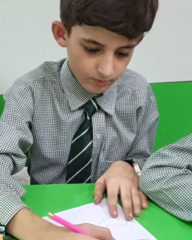 An older pupil in shirt and striped tie concentrating on a drawing at his desk