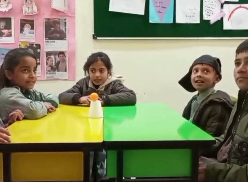 Primary pupils around classroom tables during a hands-on English lesson on prepositions