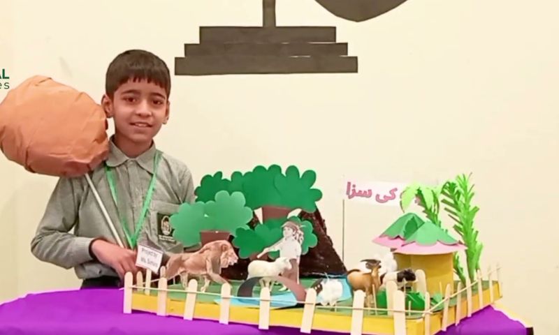 A smiling pupil presenting his handmade story diorama with model animals and trees