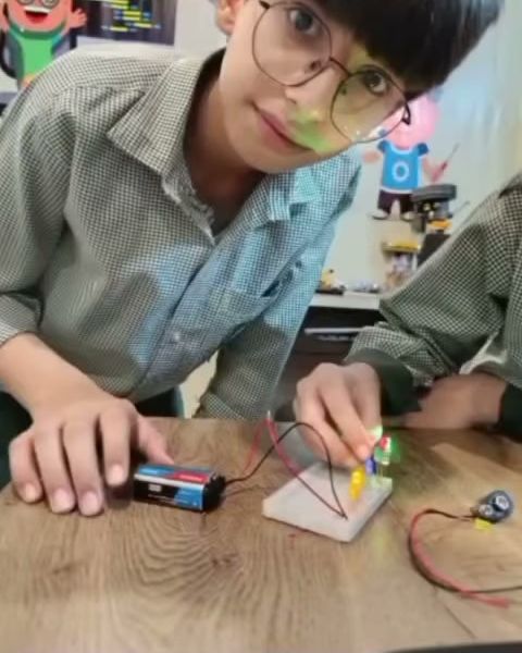 A pupil in safety glasses wiring a small LED circuit on a breadboard