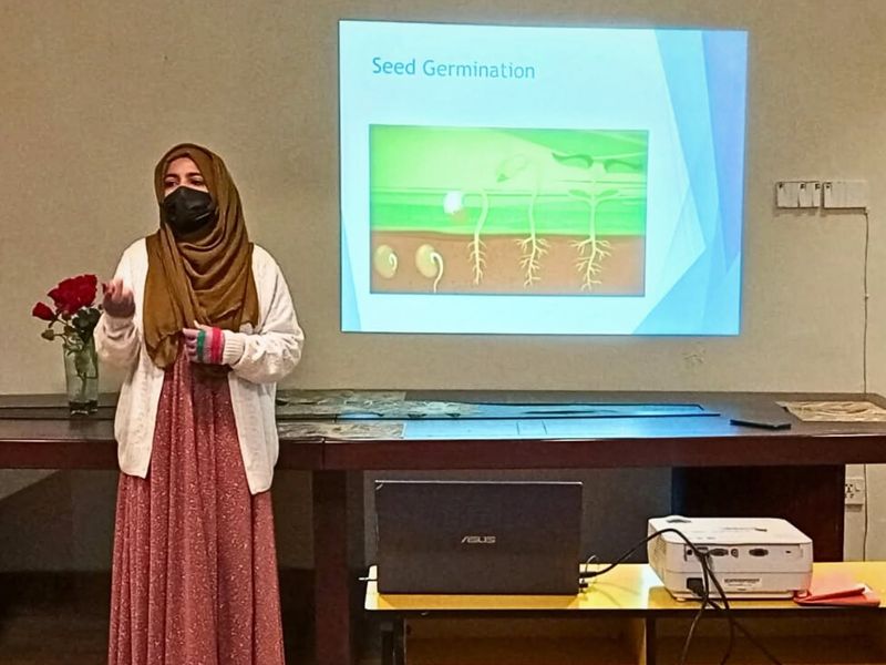 A teacher presenting a seed germination lesson on a projector screen