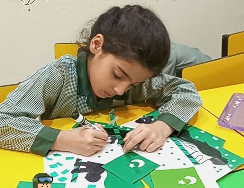 A girl carefully making a green and white Pakistan flag collage at her desk.