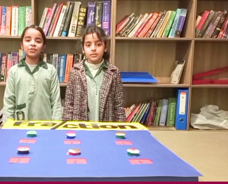 Two girls in the library presenting a fractions activity board.