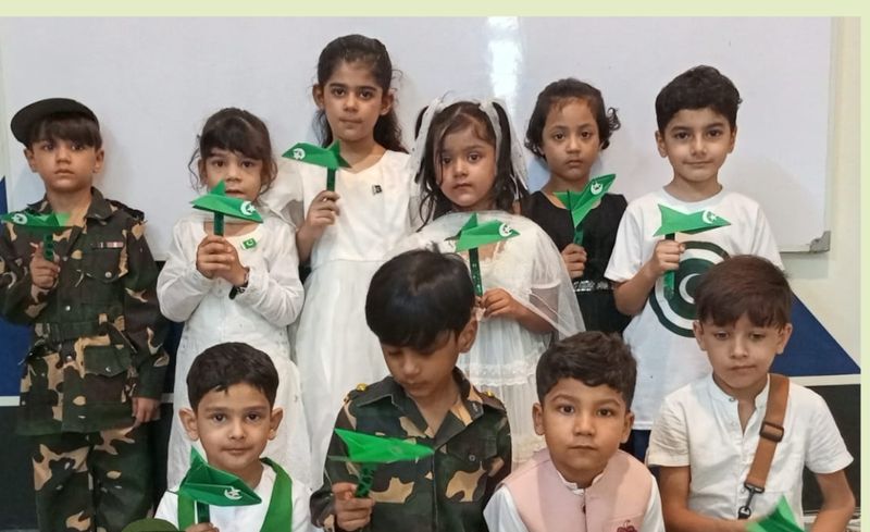 A large group of Early Years pupils in costumes holding green paper jets for Defence Day.