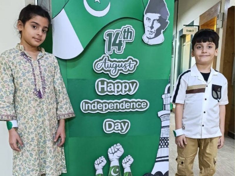 Two pupils beside a Happy Independence Day standee in a school corridor.
