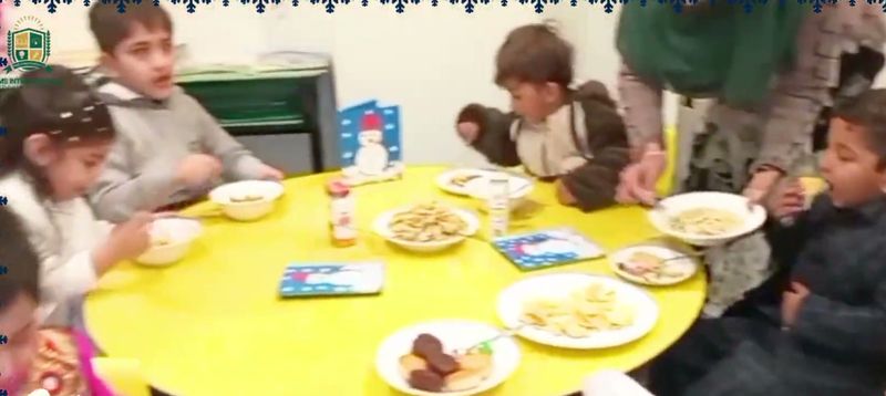 Early Years children sharing a winter lunch around a round yellow table.