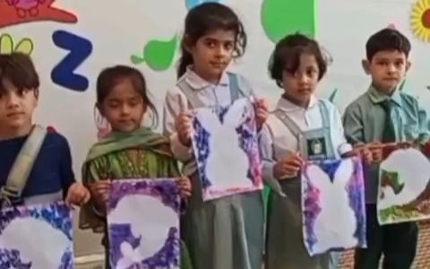 Nursery pupils in uniform proudly holding up their hand-painted artwork in front of a colourful alphabet wall.