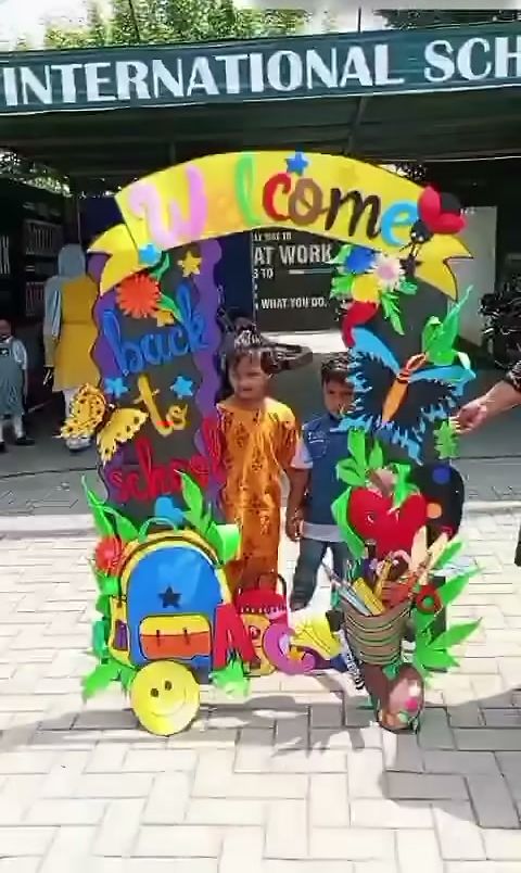 Two young pupils standing under a colourful Welcome back to school arch at the school entrance.