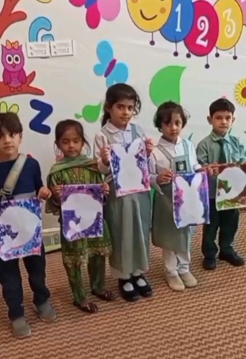 Nursery pupils in uniform holding up their hand-painted artwork in front of a colourful alphabet wall.
