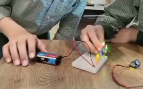 A Primary pupil's hands connecting a battery and a glowing LED on a breadboard during a robotics activity.